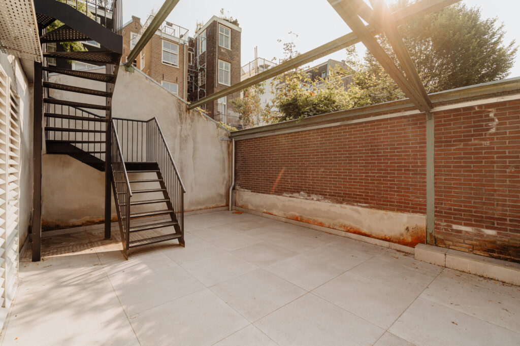 Buitenruimte met betegelde vloer, bakstenen muur en zwarte metalen trap aan de Plantage Middenlaan.